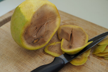 Rotten decomposing mango fruit cut up on chopping board in kitchen with knife