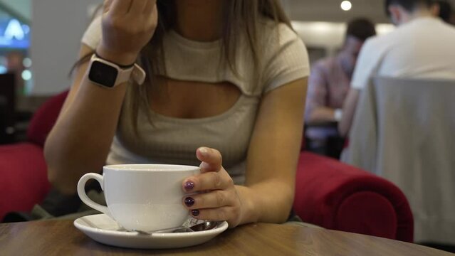 Unrecognizable young woman drinking coffee. Anonymous girl stirring the coffee with a stick and tasting the delicious foam.