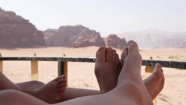 Bare feet on a bedside table on the terrace of a Bedouin camp in the desert of Wadi Rum, Jordan. Video of the feet of a heterosexual couple united and relaxed enjoying the magnificent views.