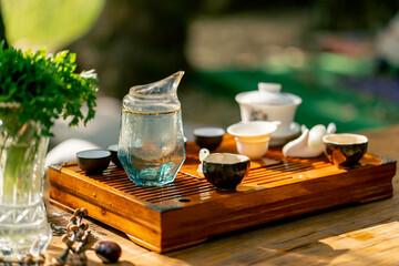 A wooden stand with bowls filled with water and cups of tea stands on table among greens and...