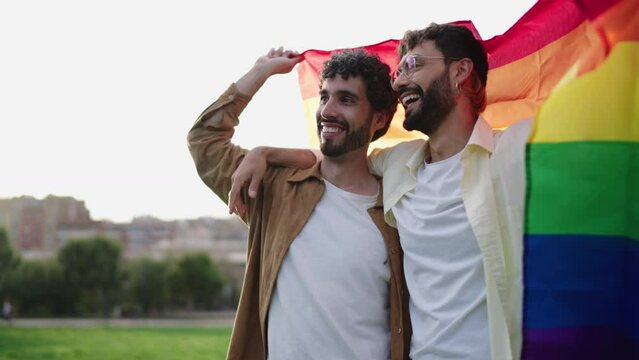 Two men lovingly wrapped in rainbow flag, sharing moment of joy and pride under an sky, symbol of LGBTQ+ unity and love. Gay couple smiling, freedom and happiness, celebrating diversity and acceptance