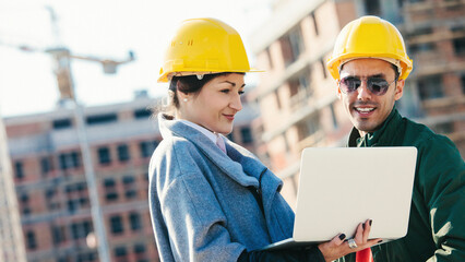 Engineers at construction site using laptop and smiling