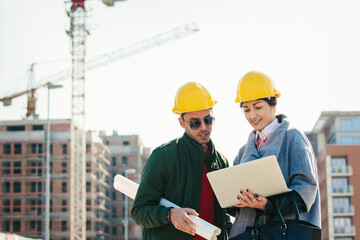 Young engineers at construction site using laptop and smiling