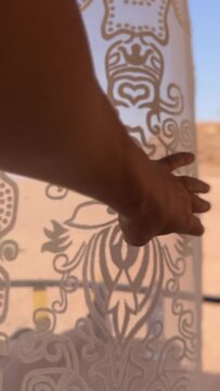 POV of a person pulling back the curtains of a hut to show the desert of Wadi Rum, Jordan. Young girl sitting on the terrace of a private tent in the middle of the desert taking pictures with her mobi