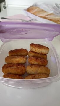 Mom's homemade fried croquettes in a tupper. Hands of unrecognizable young person opening a plastic container with food inside.