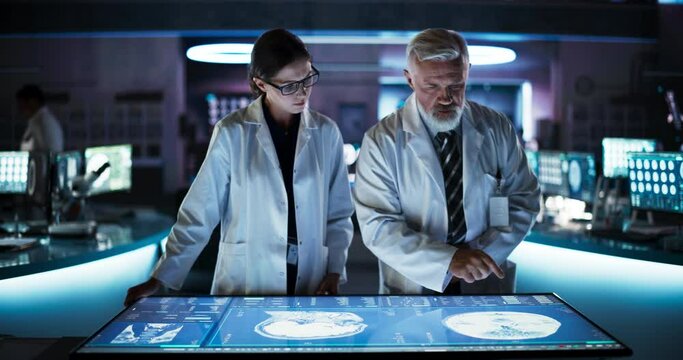 Modern Hospital Medical Cancer Research Center: Caucasian Female Neuroscientist And Male Surgeon Talking, Using Interactive Touch Screen Table With CT Scan Of Human Brain With Tumor, Finding Treatment
