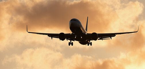 Silhouette passenger airplane. Front of silhouette airplane is flying in the orange sky with clouds, Passenger aircraft is landing. Commercial plane