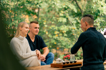 A young couple a guy and a girl are sitting at a tea ceremony and listening carefully to tea master...