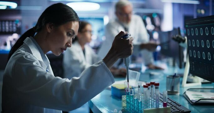 Biotechnology Research Laboratory: Two Caucasian Doctors Discussing CT Brain Scan On Computer. Focus Shifting to Female Asian Scientist Working With Test Tubes To Study Innovative Alzheimer's Medicine