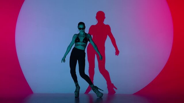 Appealing woman dancing modern choreography in leather top on high heels in the studio in red spotlight neon background.