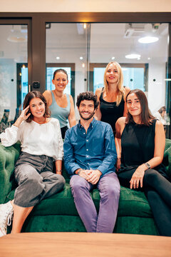 Group of optimistic young coworkers in casual outfits gathering together on comfortable sofa and looking at camera while having meeting in contemporary workspace.