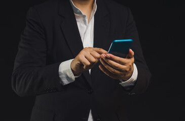 Businessman using a smartphone while standing on a black background.