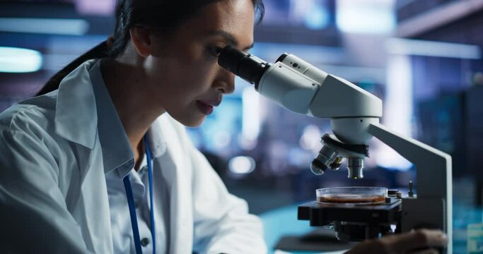 Medical Development Laboratory: Portrait of Asian Female Scientist Using Microscope, Analyzes Petri Dish Sample. Big Pharmaceutical Lab doing Medicine, Biotechnology, Microbiology, Drugs Research.