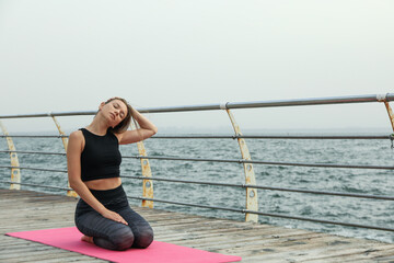 Fototapeta na wymiar Woman on yoga mat on wooden floor at sea, space for text