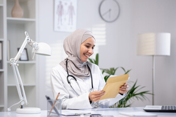 Joyful female doctor in hijab received envelope message mail notification with good results of...