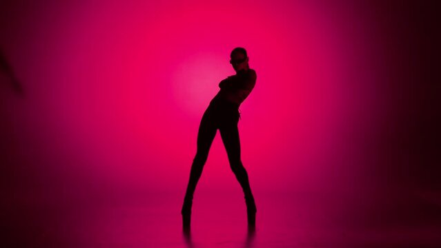 Silhouette of attractive woman dancing modern choreography on high heels in the studio on electric pink neon background.