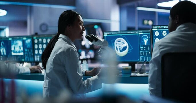 Female Asian Neuroscientist Using Microscope And Discussing Finding With Black Doctor In Medical Research Center. Specialist Studying Human Brain To Develop Life-Saving Medication For Patients.