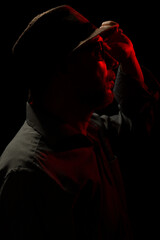 Discreet portrait of man wearing hat and sunglasses in darkness with red light on face.