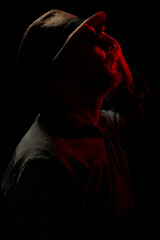 Discreet portrait of man wearing hat and sunglasses in darkness with red light on face.