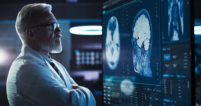 Medical Research Center: Close-Up Portrait Of Caucasian Male Neurologist, Neuroscientist, Neurosurgeon, Looks at TV Screen with Brain MRI Scan Images, Thinks about Sick Patient Treatment Method.