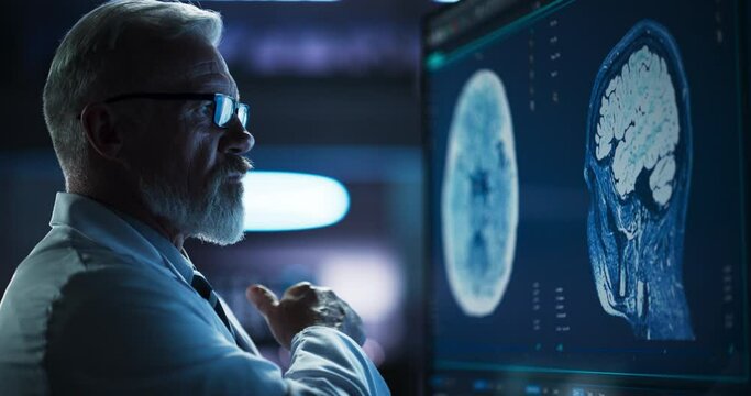 Medical Research Center: Close Up Portrait Of Caucasian Male Neurologist, Neuroscientist, Neurosurgeon, Looks at TV Screen with Brain MRI Scan Images, Thinks about Sick Patient Treatment Method.