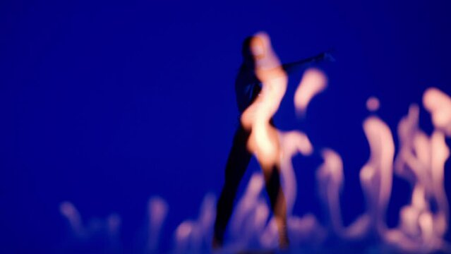 Silhouette of beautiful woman dancing dynamic choreography on high heels in the studio on blue background with flames.