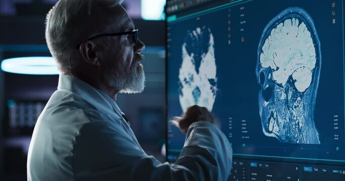 Medical Research Center: Close-Up Portrait Of Caucasian Male Neurologist, Neuroscientist, Neurosurgeon, Looks at TV Screen with Brain CT Scan Images. Doctor Thinks about Sick Patient Treatment Method.