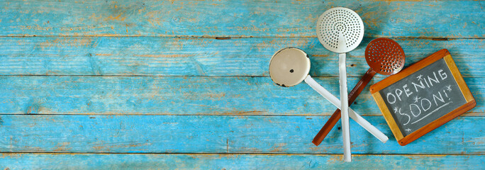 Restaurant opening soon with vintage kitchen utensils and message on blackboard, large free copy space. Panoramic format.