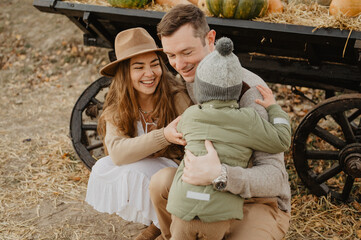 Young mom and dad with their little son hugging and walking on a pumpkin farm. Autumn.