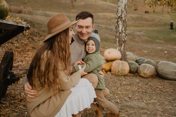Young mom and dad with their little son hugging and walking on a pumpkin farm. Autumn.