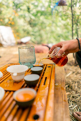 Close-up shot of a man's hand pouring brewed natural tea into ceramic bowls lined up in row