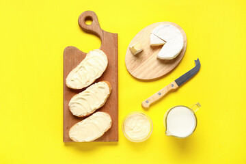 Wooden board of bread with butter and camembert on yellow background