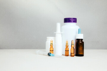 A set of medicines for treatment in bottles and a syringe with ampoules for injections on a light background. Front view