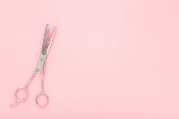 New professional hair thinning scissors on light pink table background. Pastel color. Closeup. Empty place for text. Top down view.