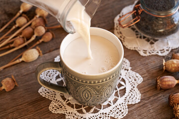 Pouring vegan poppy seed milk from a glass jug into a cup