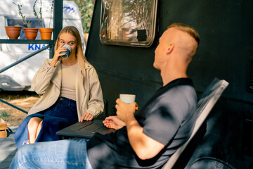 A young couple a man and a girl are drinking tea on the terrace near their motorhome in camper