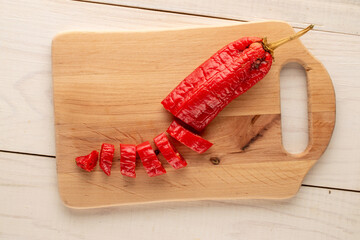 One red hot pepper cut into pieces on a wooden kitchen board, macro, top view.