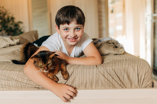 Kid boy hugs a red fluffy cat indoors lifestyle authentic image indoors in cozy home. Love domestic animals pets