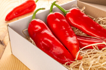Several red sweet peppers with paper box on wooden table
