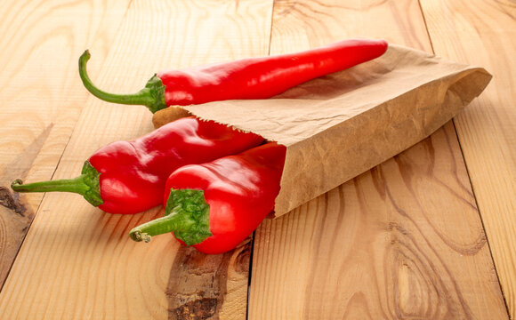 Three red sweet peppers with a paper bag on a wooden table