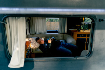 A tired sad man lies depressed on the sofa by the trailer window and looks indifferently at screen...