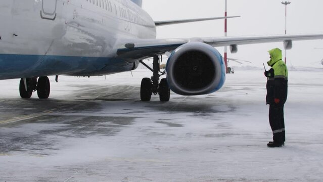 Winter Skies: A Man Standing in Front of an Airplane on a Snowy Runway