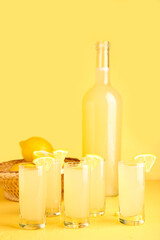 Shots and bottle of tasty Limoncello on yellow background