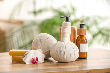 Herbal massage bags, bottles of cosmetic products and soap bars on wooden table - obrazy, fototapety, plakaty