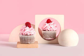 Decorative stand with tasty raspberry cupcakes on pink background