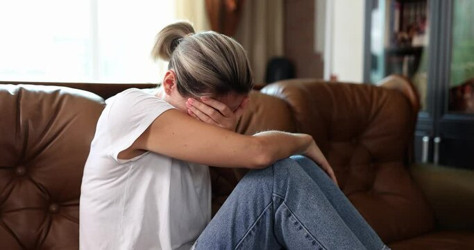 A young woman cries at home on a leather sofa, a close-up, slowmotion. Concepts loss, resentment shallow focus