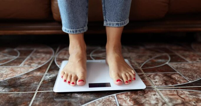 Female legs in jeans stand on electronic scales, close-up. Diet control. Weight measurement concept