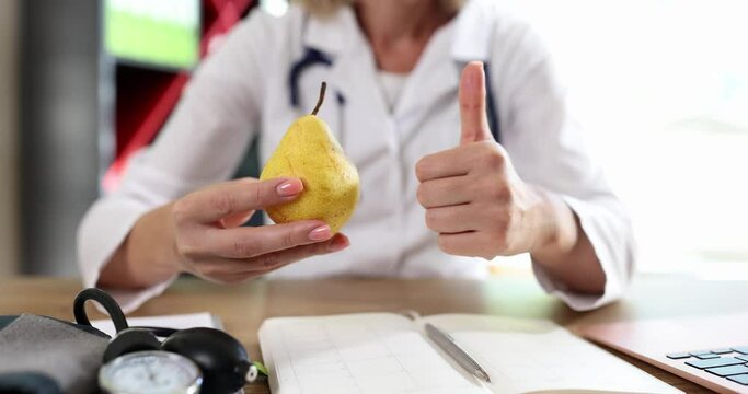 Young female hands of the doctor hold the fruit and show the gesture to the finger up, close-up. Concept Vitamin diet
