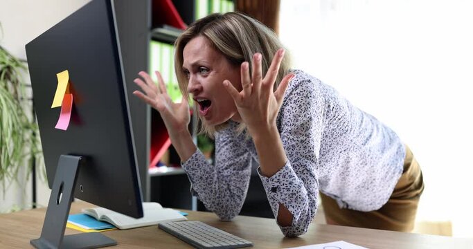 A young woman in the office at a computer monitor grabs her head, close-up. Business error, problematic at work