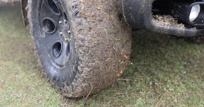 Close-up car with a dirty wheel on the grass, slowmotion. Road without asphalt, the front of the SUV in the swamp
